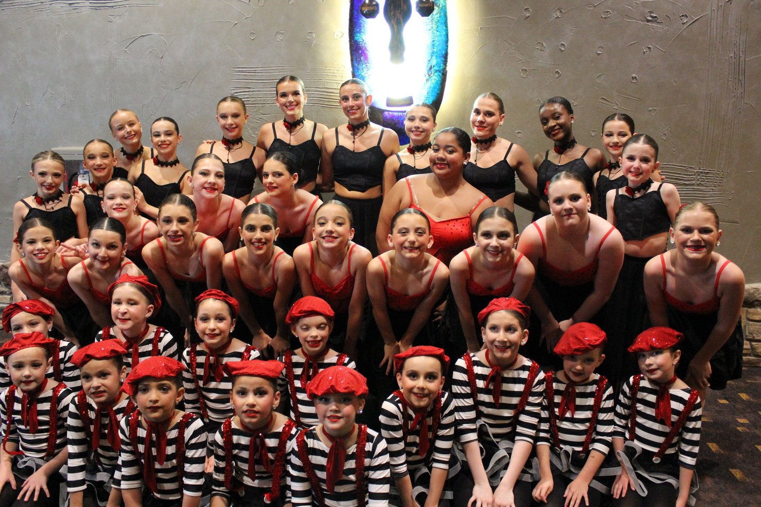 The 2025-26 production cast in coordinated red, black, and striped costumes.